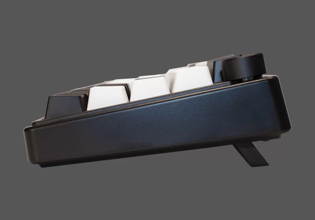 Vista lateral del teclado mecánico Okami EX65 mostrando su inclinación ergonómica y soporte ajustable.