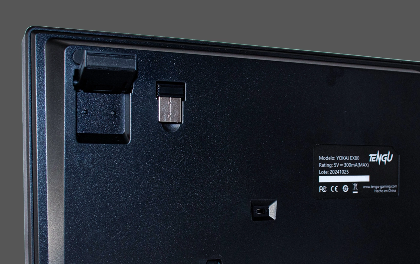 Parte inferior del teclado Yokai EX80 mostrando el dongle USB integrado, soporte ajustable y etiqueta técnica.